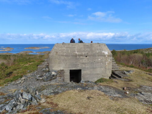 Utvorda kystfort, to personer på toppen av en bunkers, med havet og blå himmel i bakgrunn