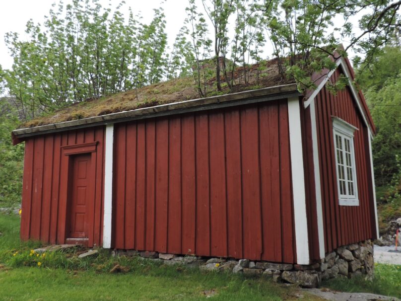 Bygning med røde vegger, hvite kanter og torv på taket