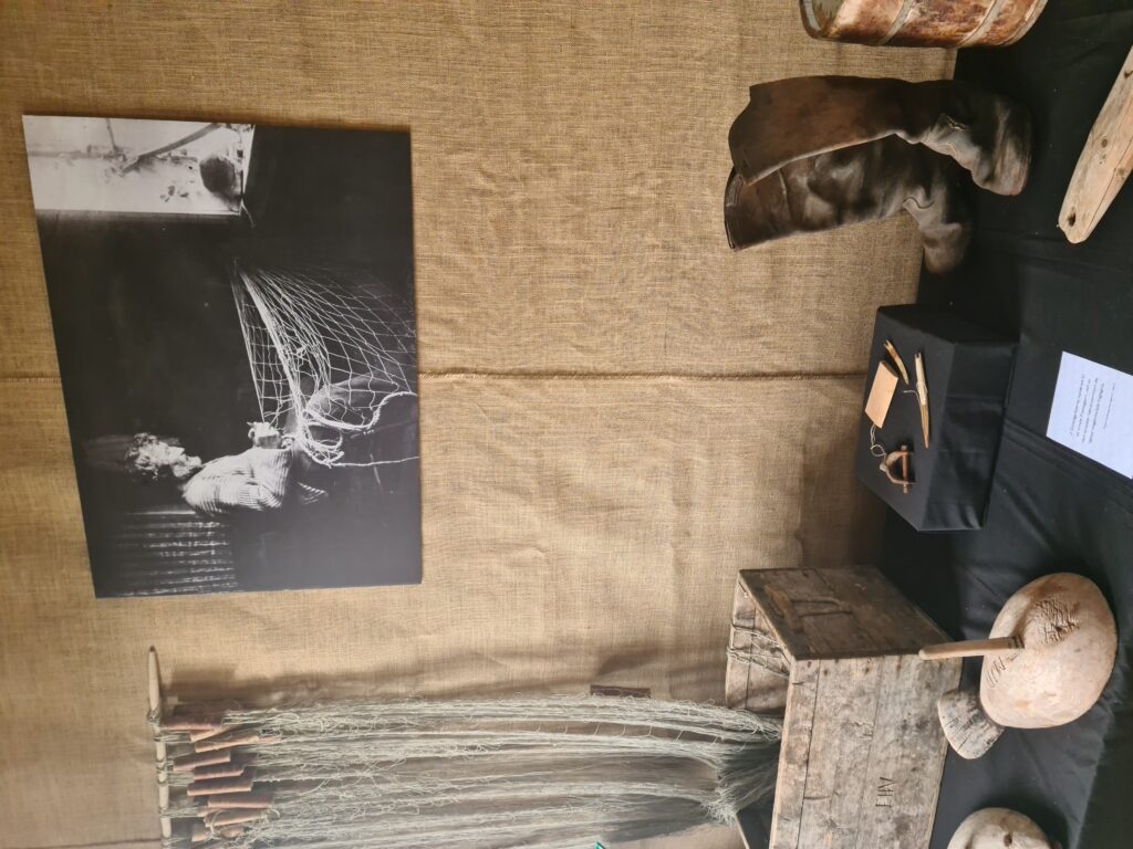 utstilling med gjenstander fra fiske og et foto i bakgrunnen som viser en eldre man som bøter garn